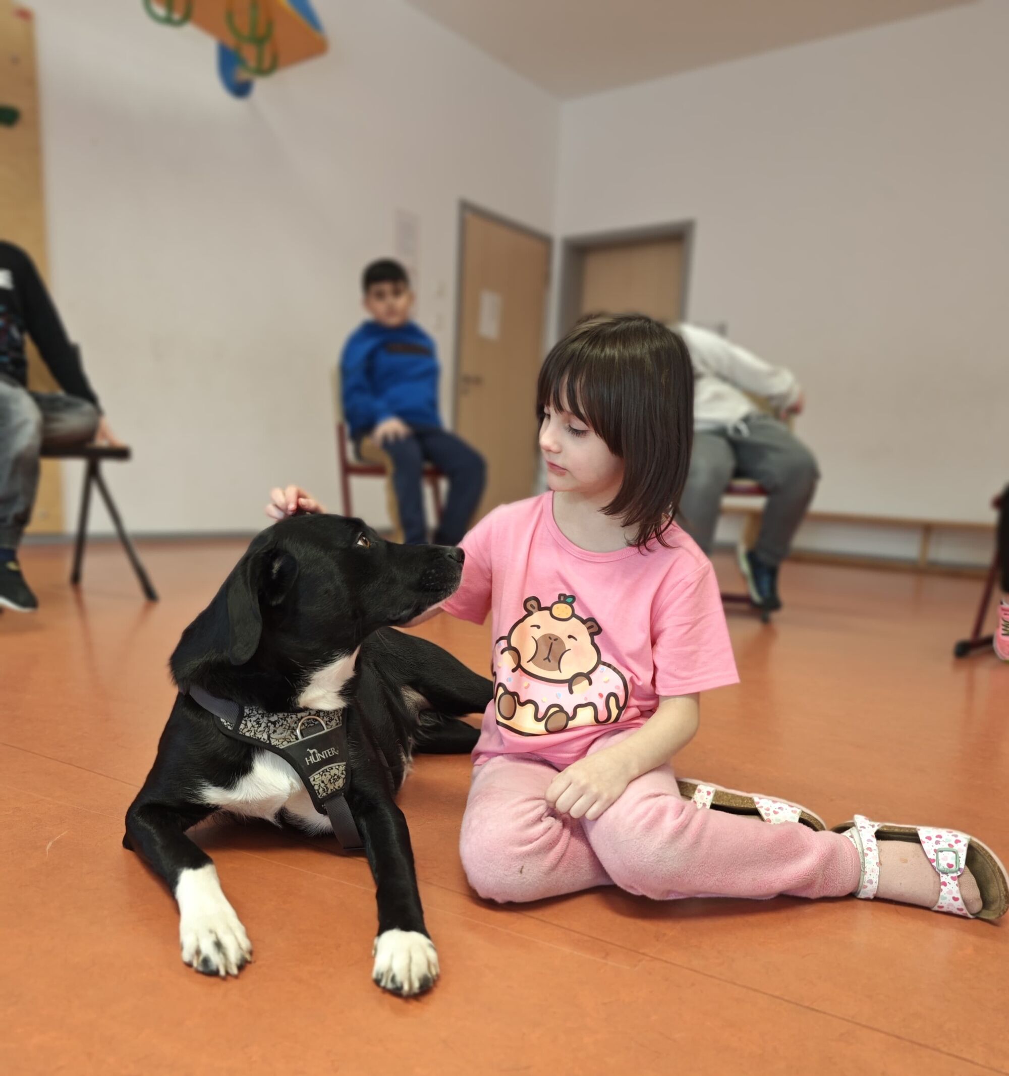 Ein M&auml;dchen sitz auf dem Boden und streichelt einen schwarzen Hund