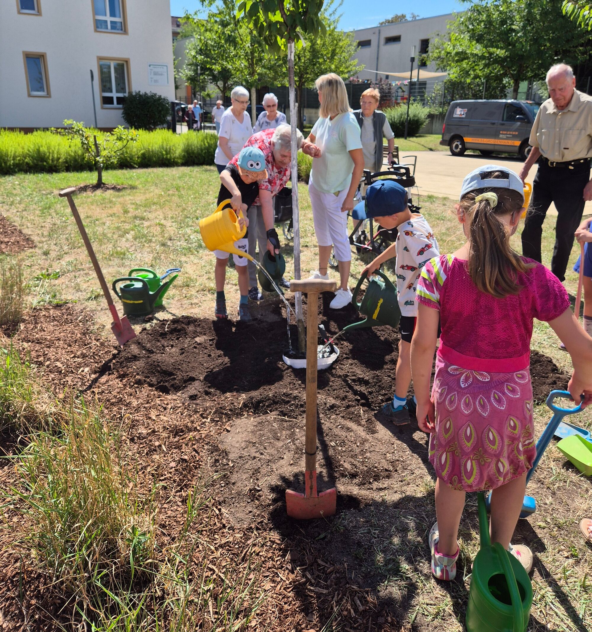 Kinder und &auml;ltere Menschen w&auml;ssern einen neu gepflanzten Baum
