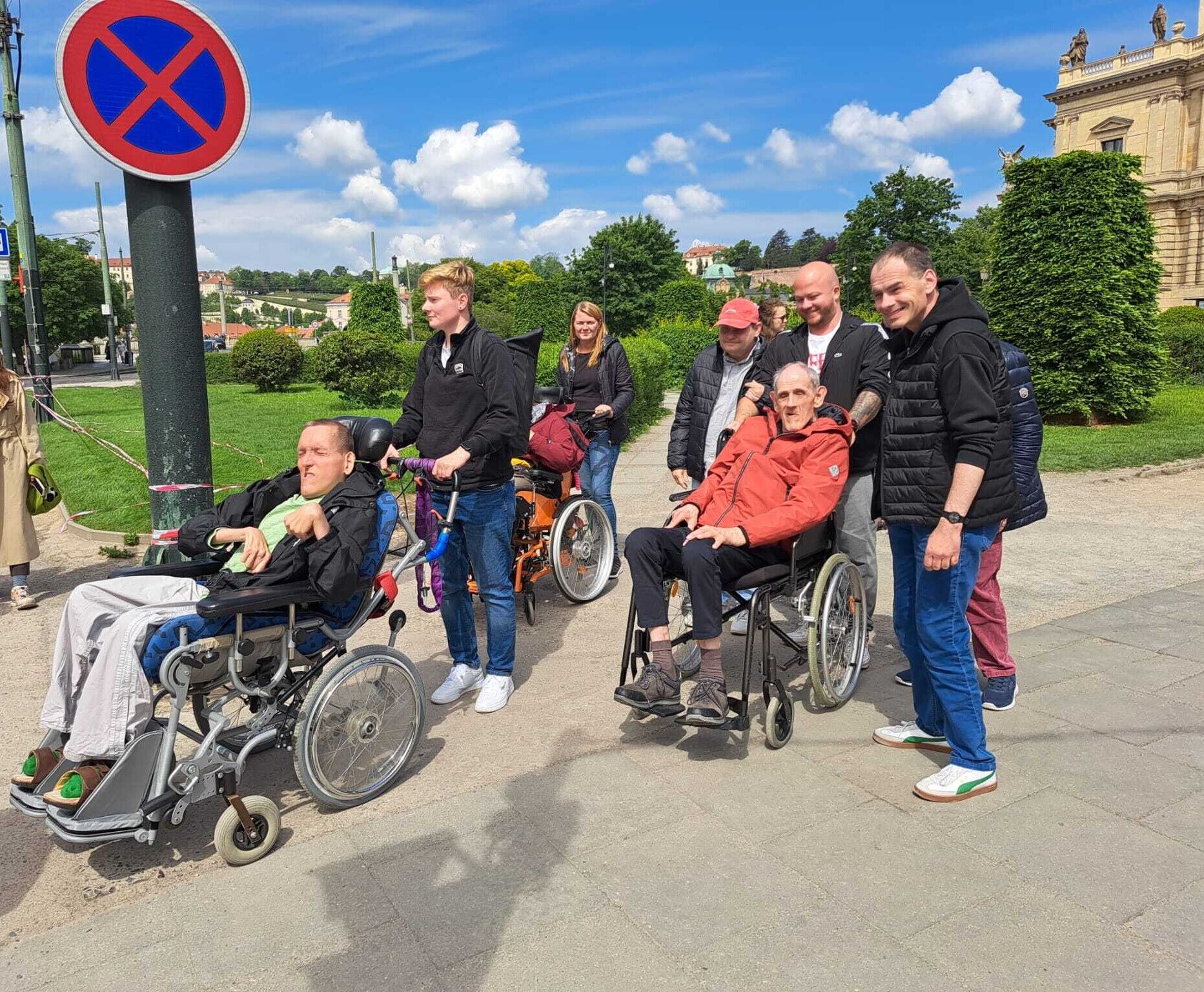© SEB Leipzig Menschen stehen, einige sitzen im Rollstuhl, auf einer Straße in einem Ort.