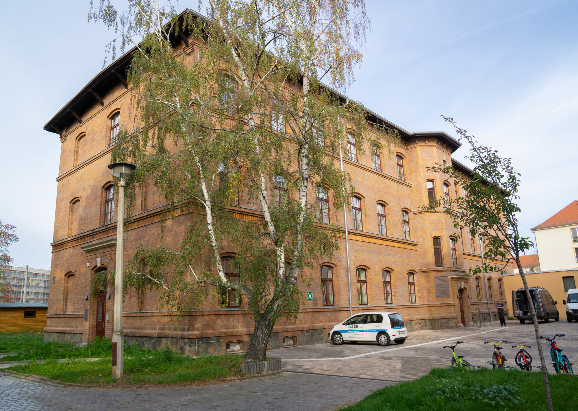 Ein großes rötliches Backsteingebäude mit großem Baum davor.
