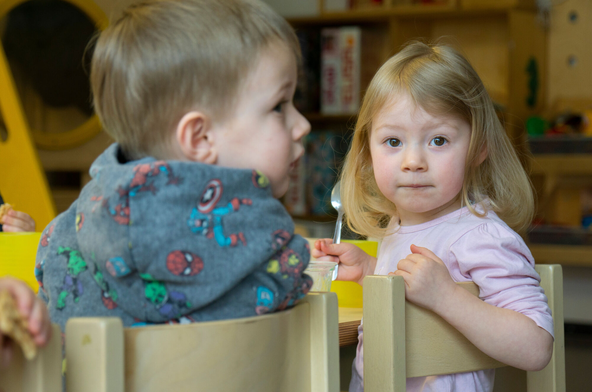 Zwei Krippenkinder sitzen an einem Tisch, ein M&auml;dchen schauet in die Kamera
