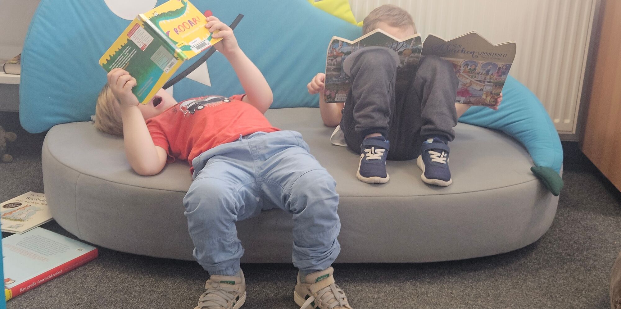 Zwei Kinder liegen auf einer Couch und sehen sich B&uuml;cher an