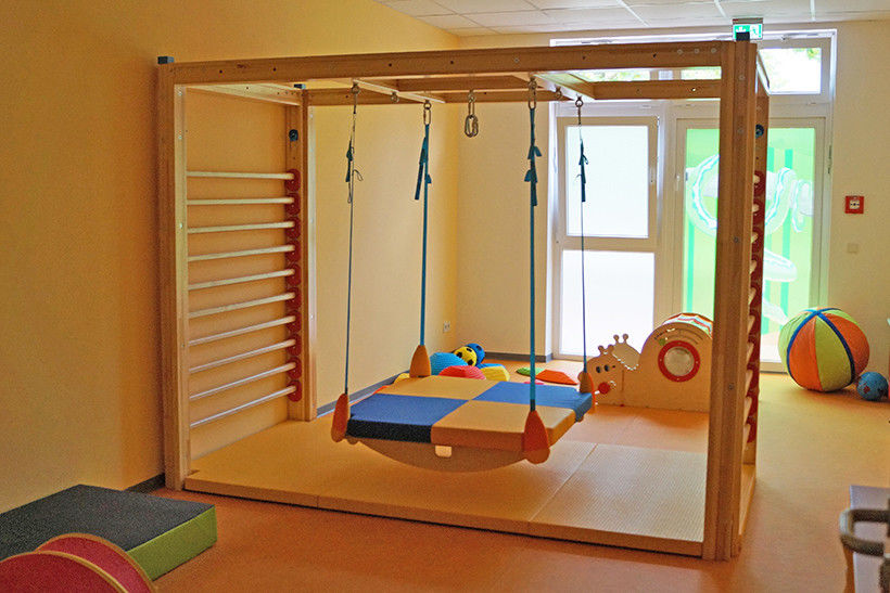 Ein großer Raum mit Sprossenwand, großer Hängeschaukel, Matten und Bällen.