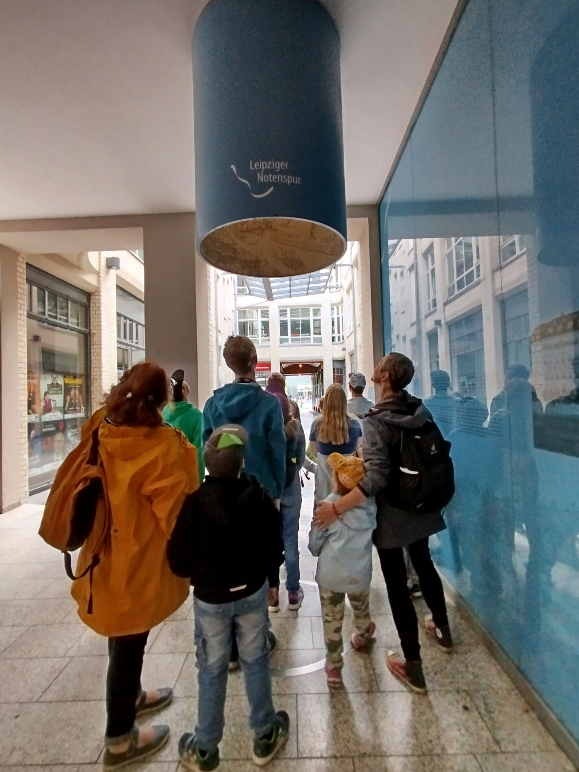 Menschen stehen neben einer blauen Wand und schauen nach oben in große Röhre