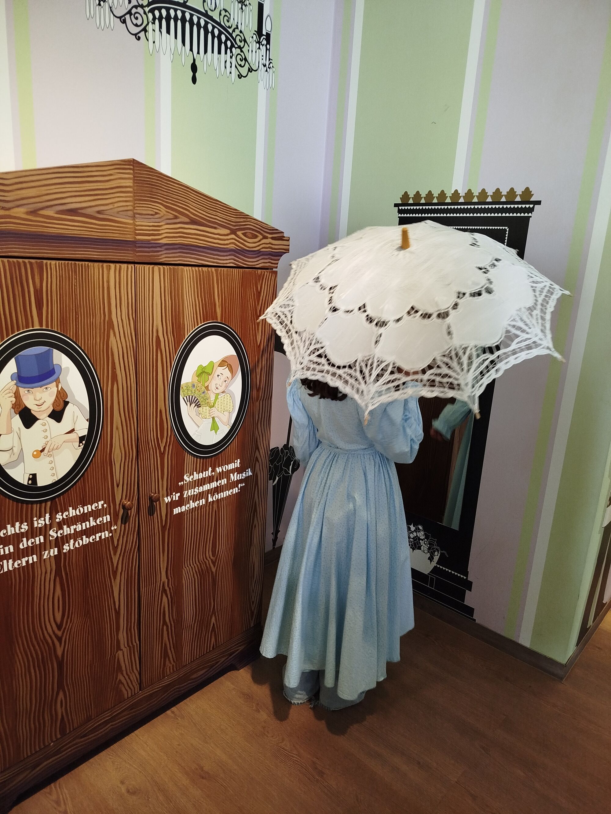 Eine M&auml;dchen steht in einem historischen Kleid und Schirm aus Spitze vor einem Spiegel