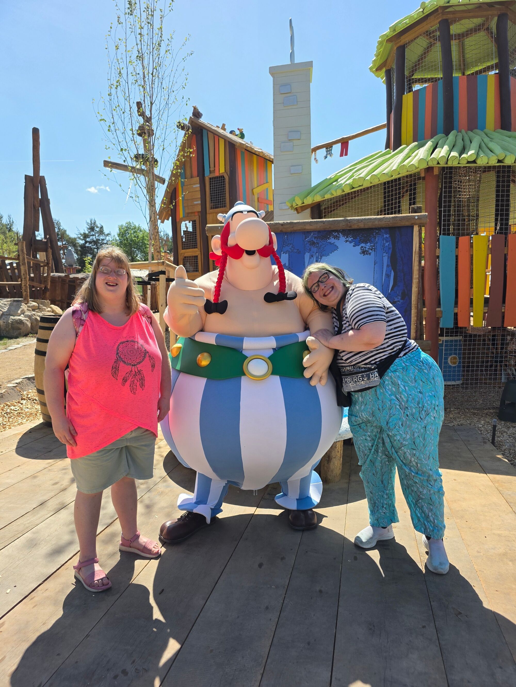 Zwei Frauen stehen mit Obelix vor einer bunten Kulisse des Belantis-Parks