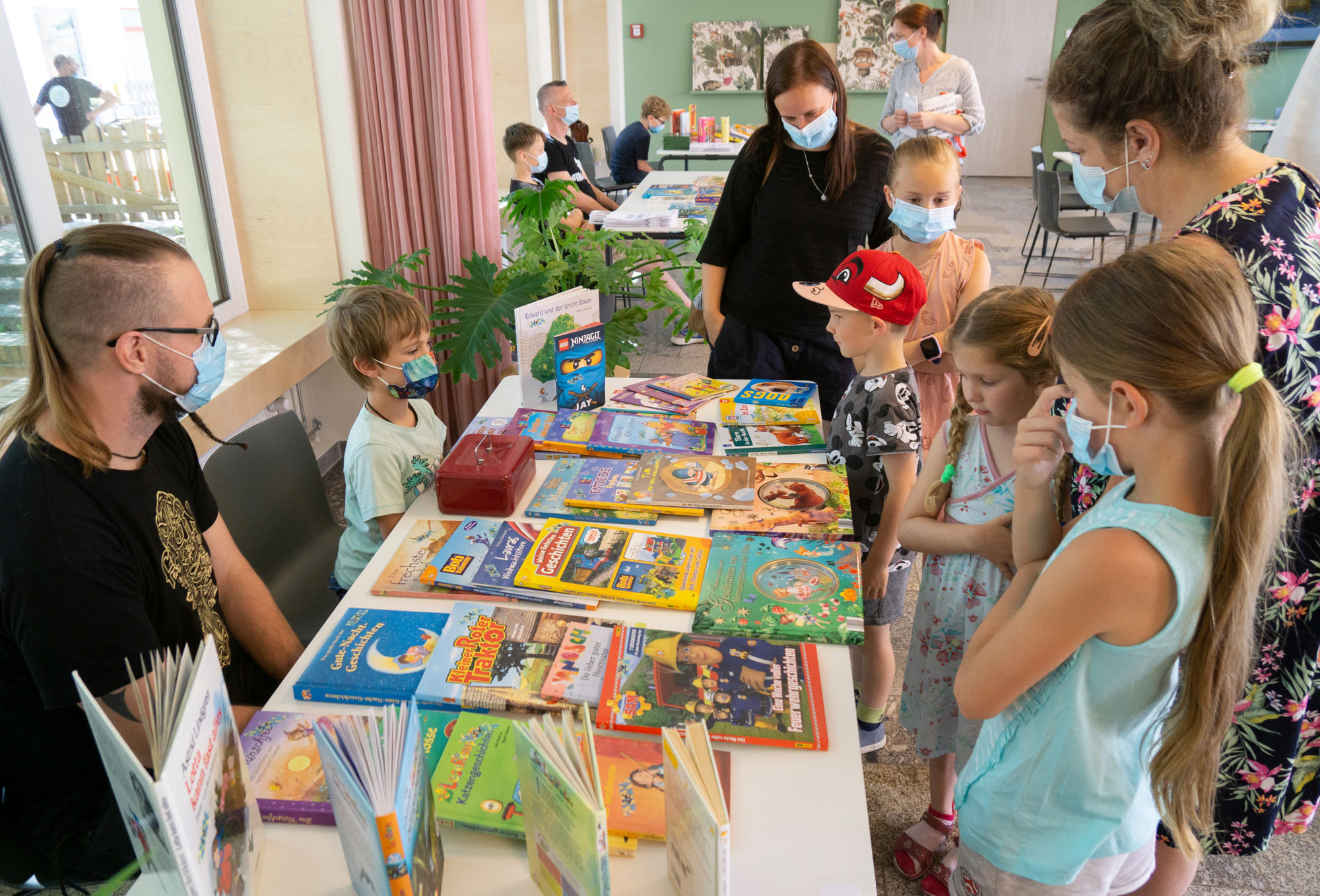 Viele Bücher liegen auf Verkaufstischen, davor stehen Kinder und Erwachsene