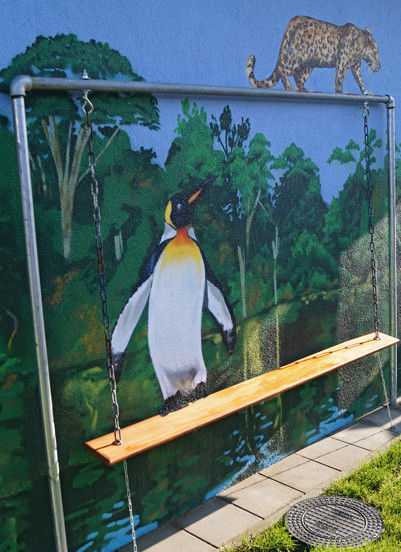 Eine bemalte Außenfassade mit Bäumen und einem Pinguin auf einer Bank.