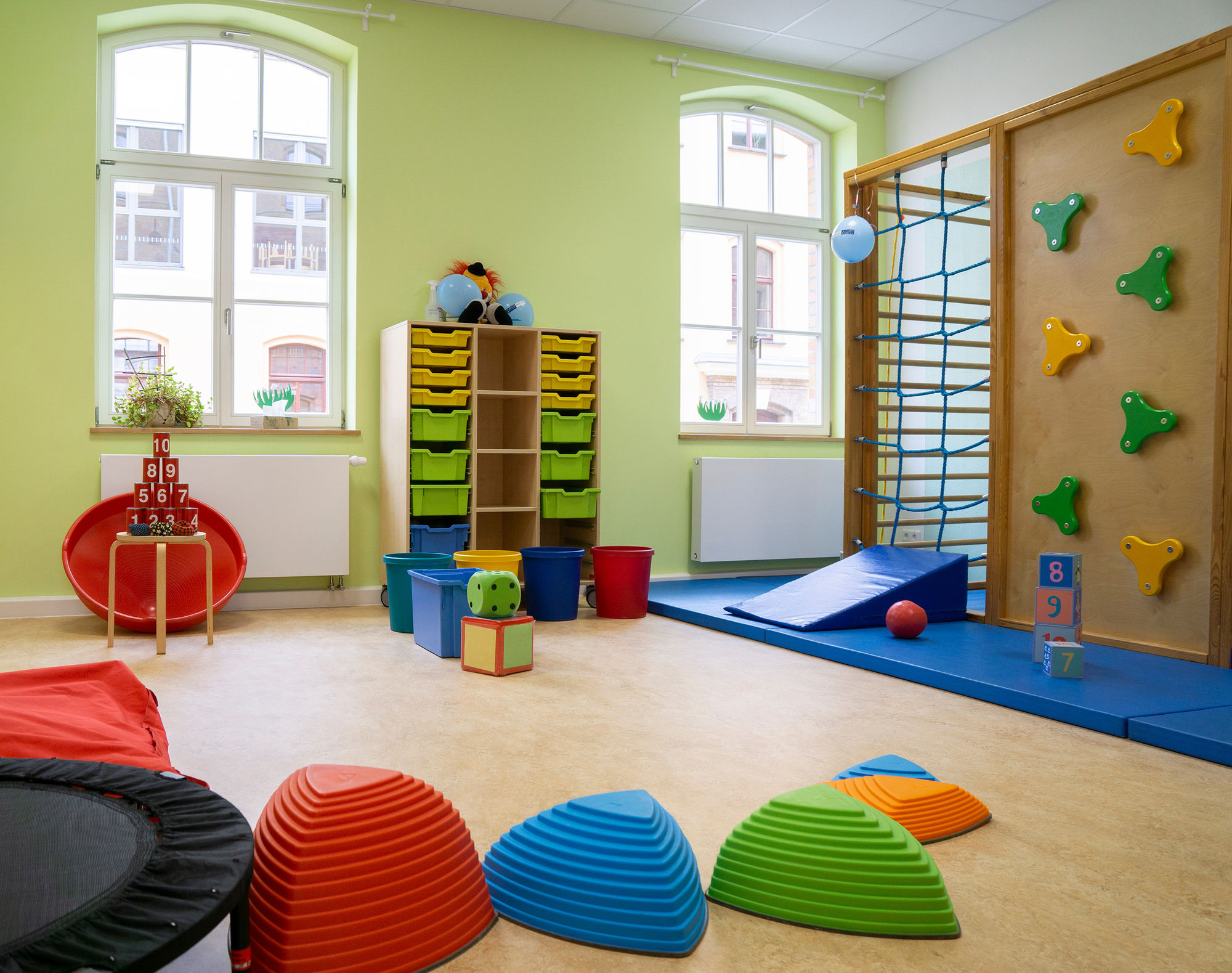 ein großer heller Raum mit Matten, Sprossenwand, Kletterwand, Kegeln, Bällen