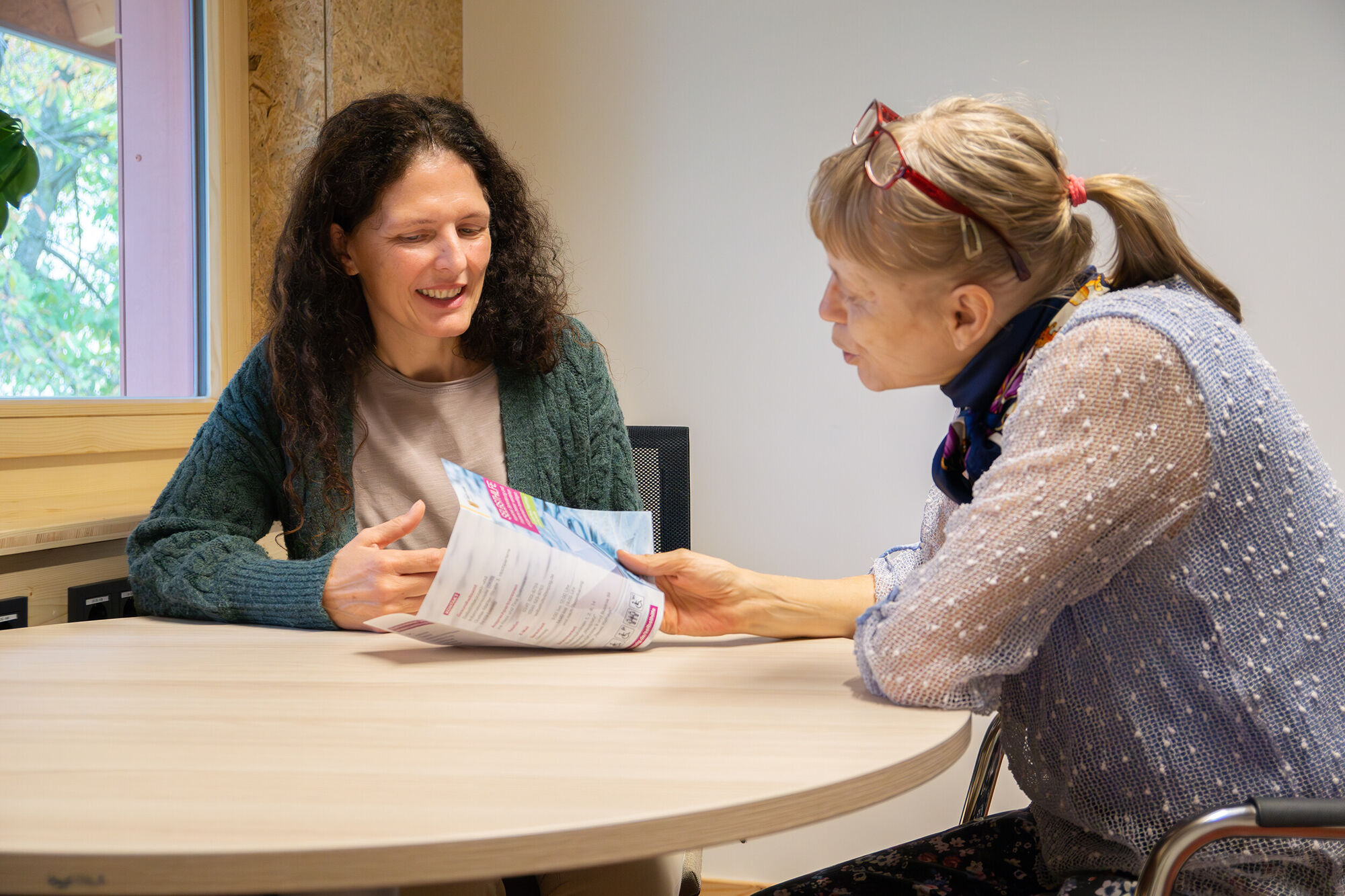 zwei Frauen sitzen an einem Tisch und reden über einen Flyer