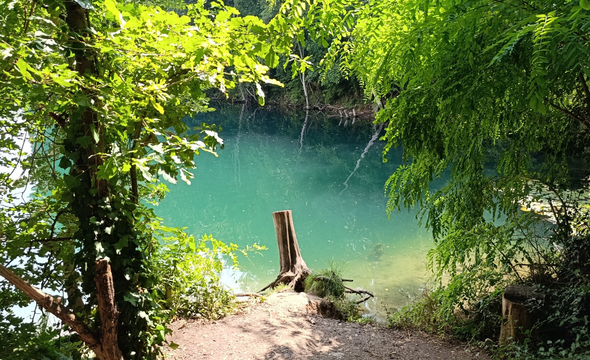 Das Ufer des Sees leuchtet t&uuml;rkis-blau in der Sonne