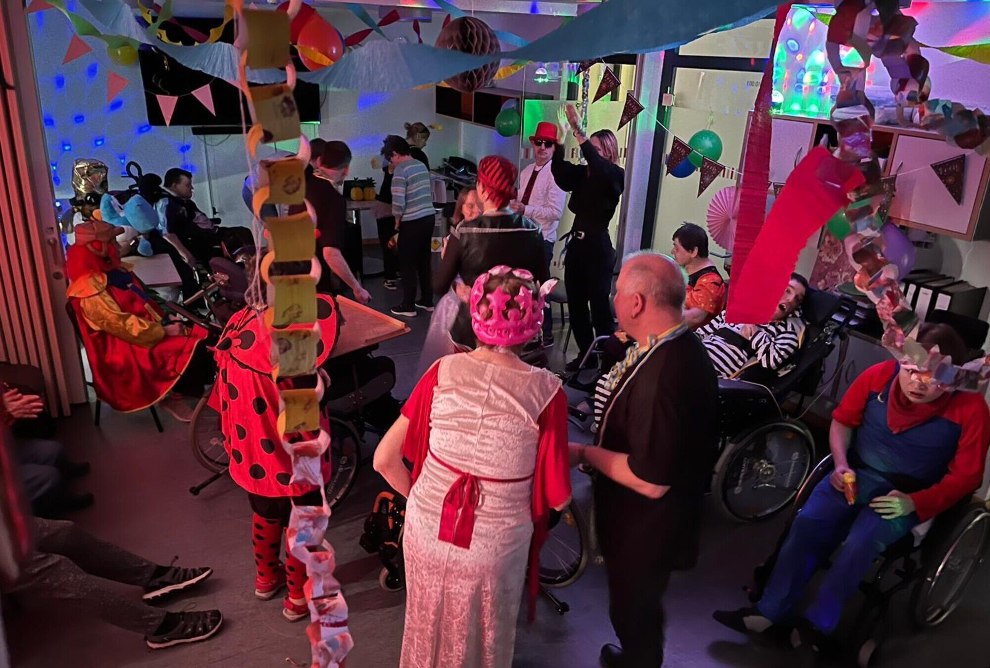 viele Menschen in Kost&uuml;men stehen in einem gro&szlig;en bunt geschm&uuml;ckten Raum