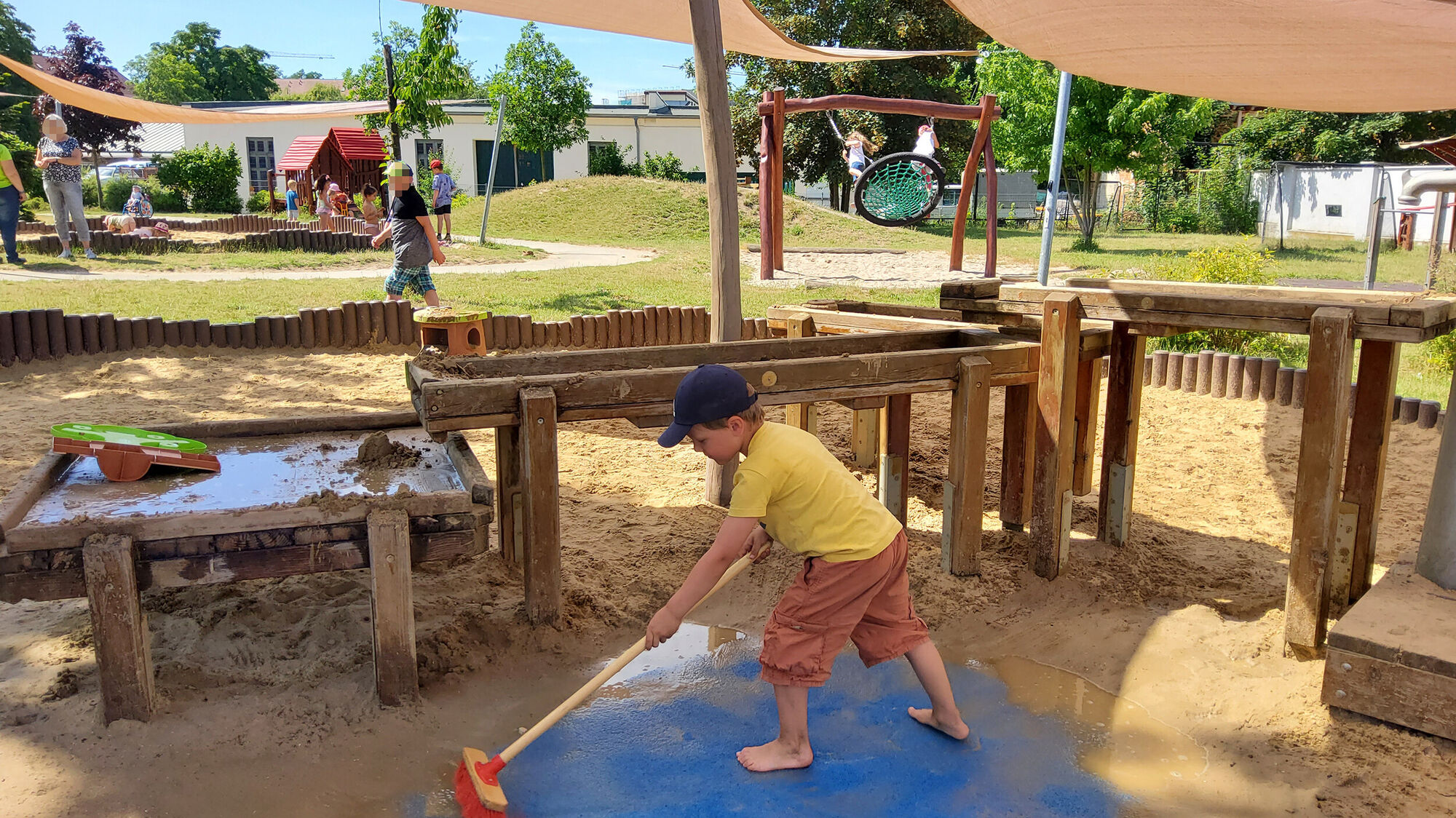 Ein Junge fegt vor einer erh&ouml;hten Sand-Matschstrecke