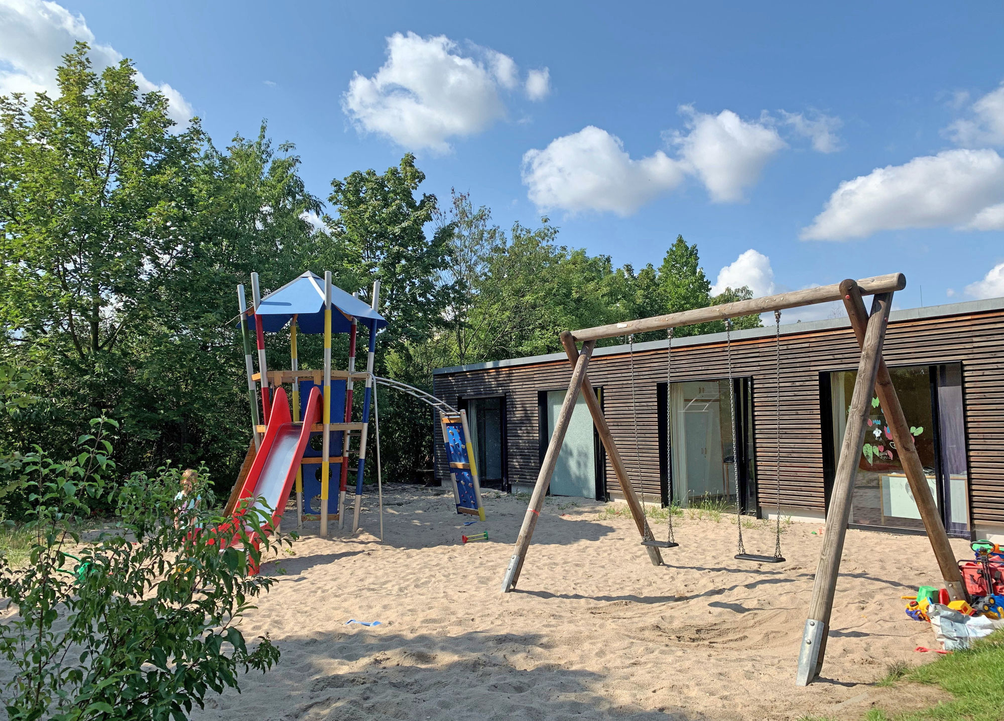 Ein Spielplatz mit Klettergerüst, Schaukeln, Rutsche, Sand und Wiese.