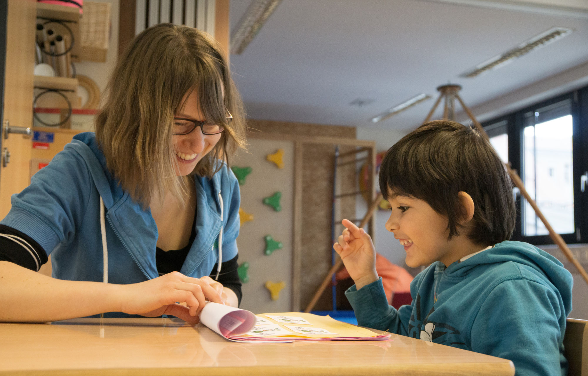 Eine Therapeutin sitzt mit einem Kind an einem Tisch und schauen sich einen H