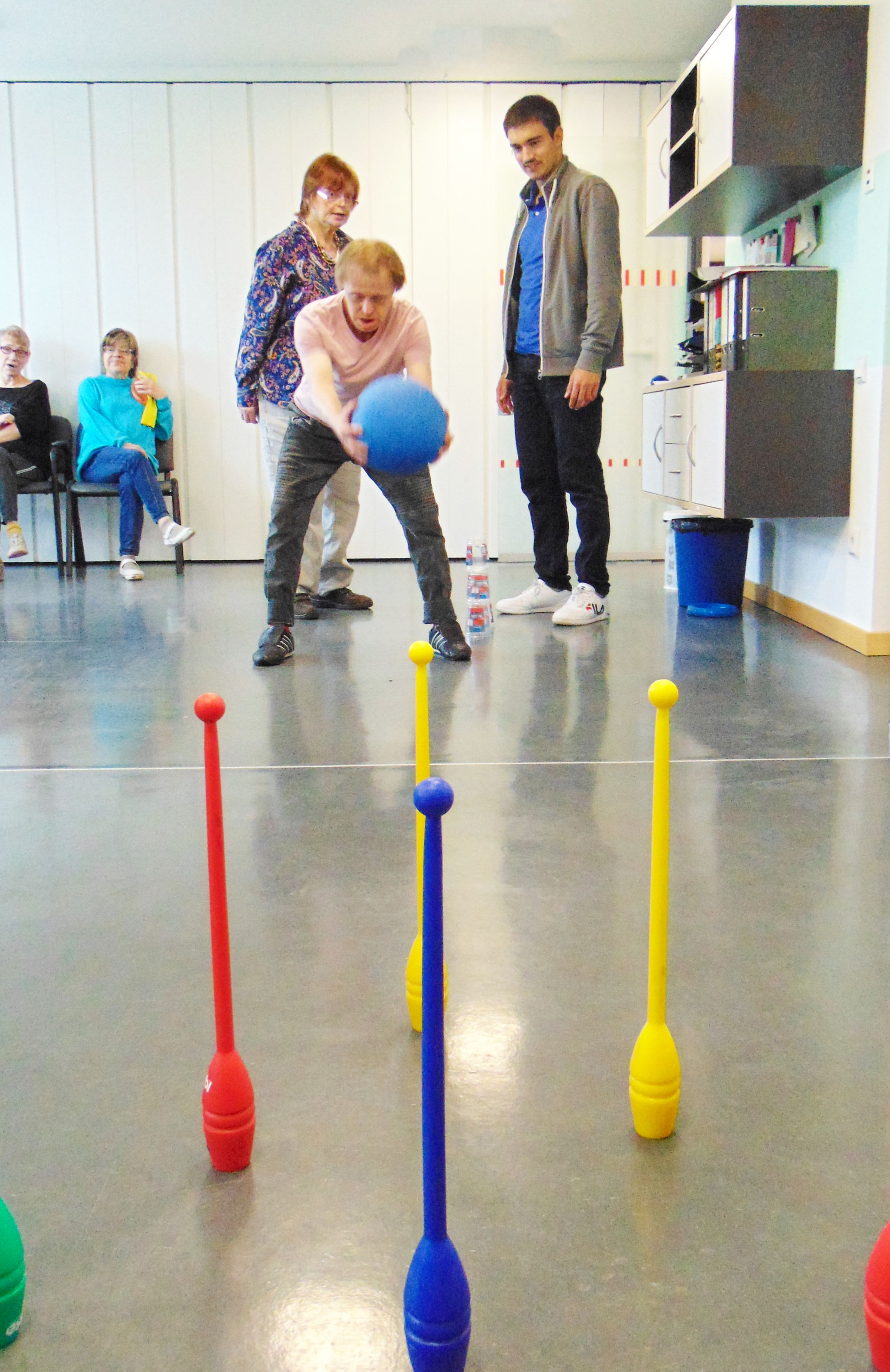 Ein Frau wirft einen blauen Ball in Richtung von aufgestellten bunten Kegeln.