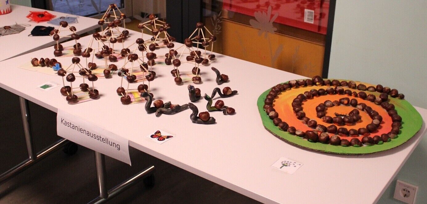 Gebastelte Kastanienfiguren auf einem Tisch. Davor ist ein Schild mit der Aufschrift Kastanienausstellung