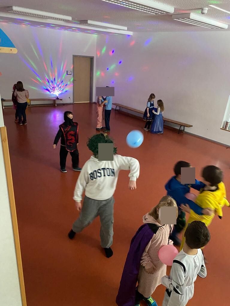 Viele Kinder in Kost&uuml;men in einem gro&szlig;en Raum mit bunten Lichtern und Luftballons.