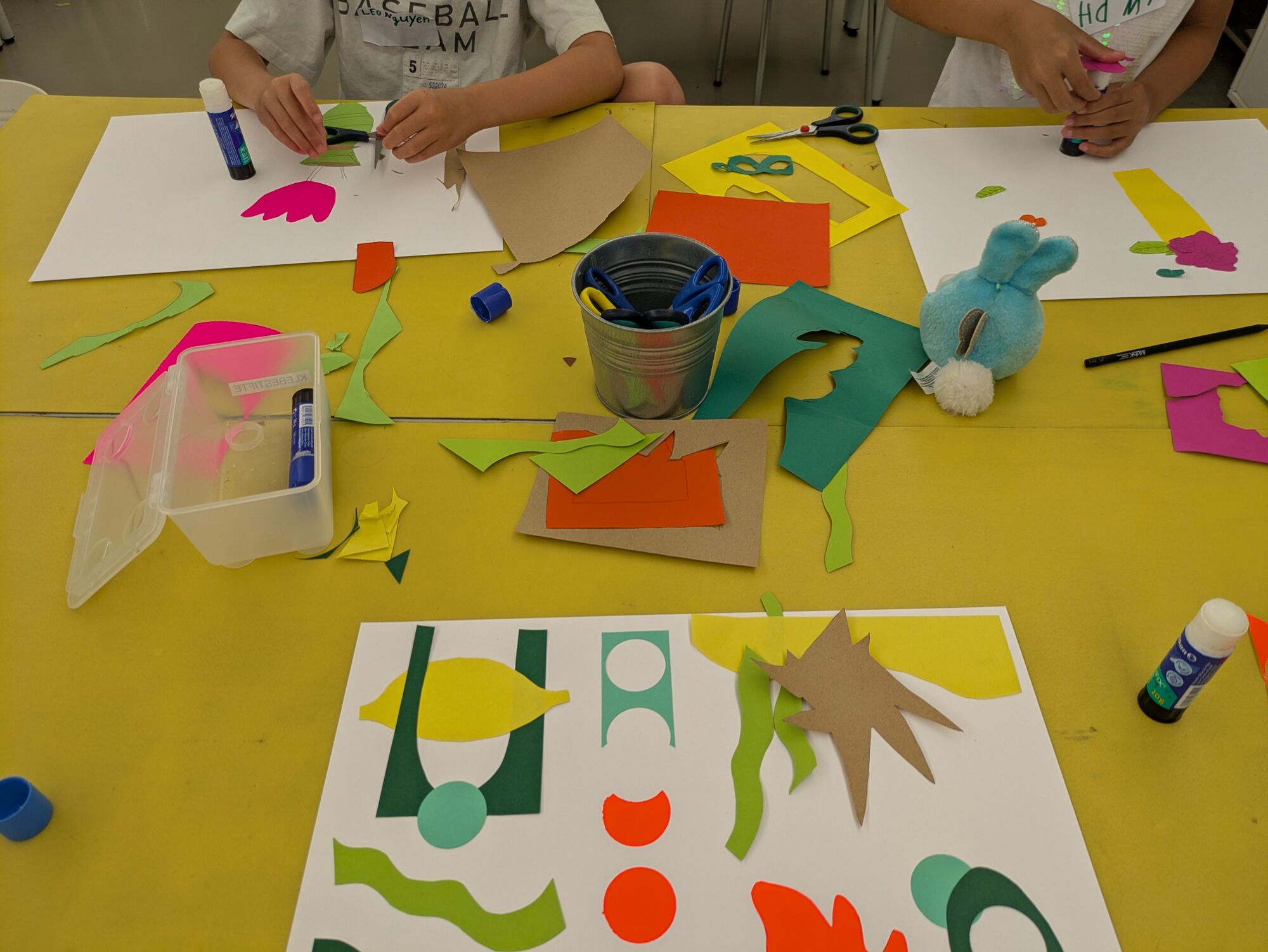Viele bunte Bastelmaterialien auf einem Tisch an dem Kinder sitzen