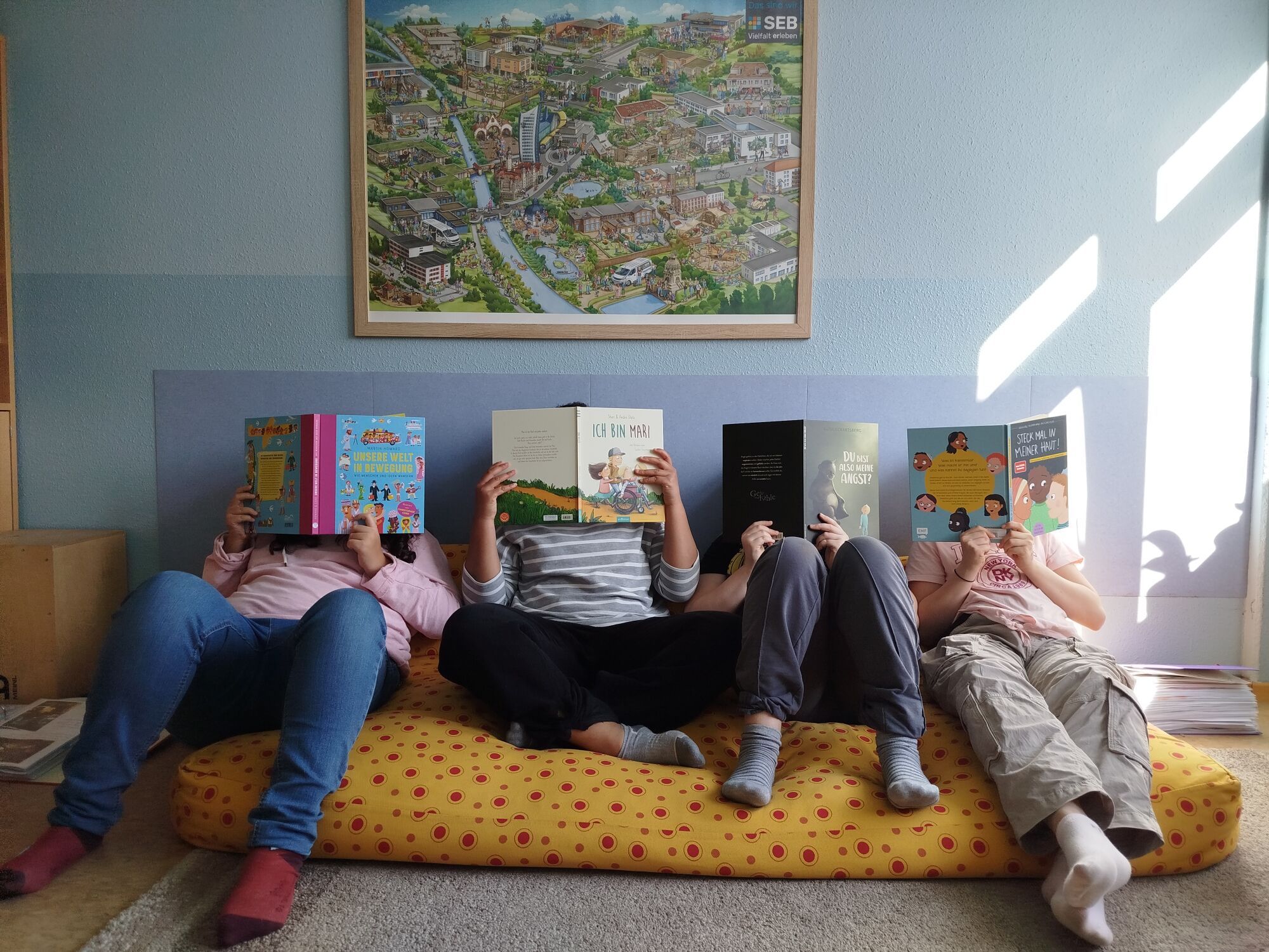 Kinder sitzen und liegen auf einem gro&szlig;en Bodenkissen und lesen B&uuml;cher